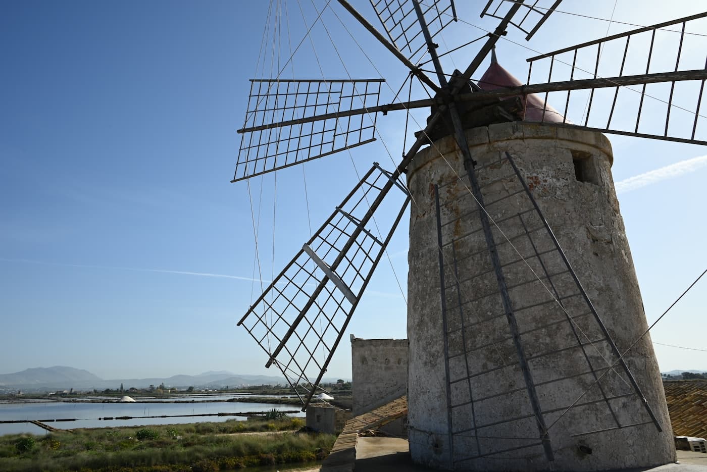 Le saline di Trapani: le vasche, un mulino a vento e le montagne dietro.